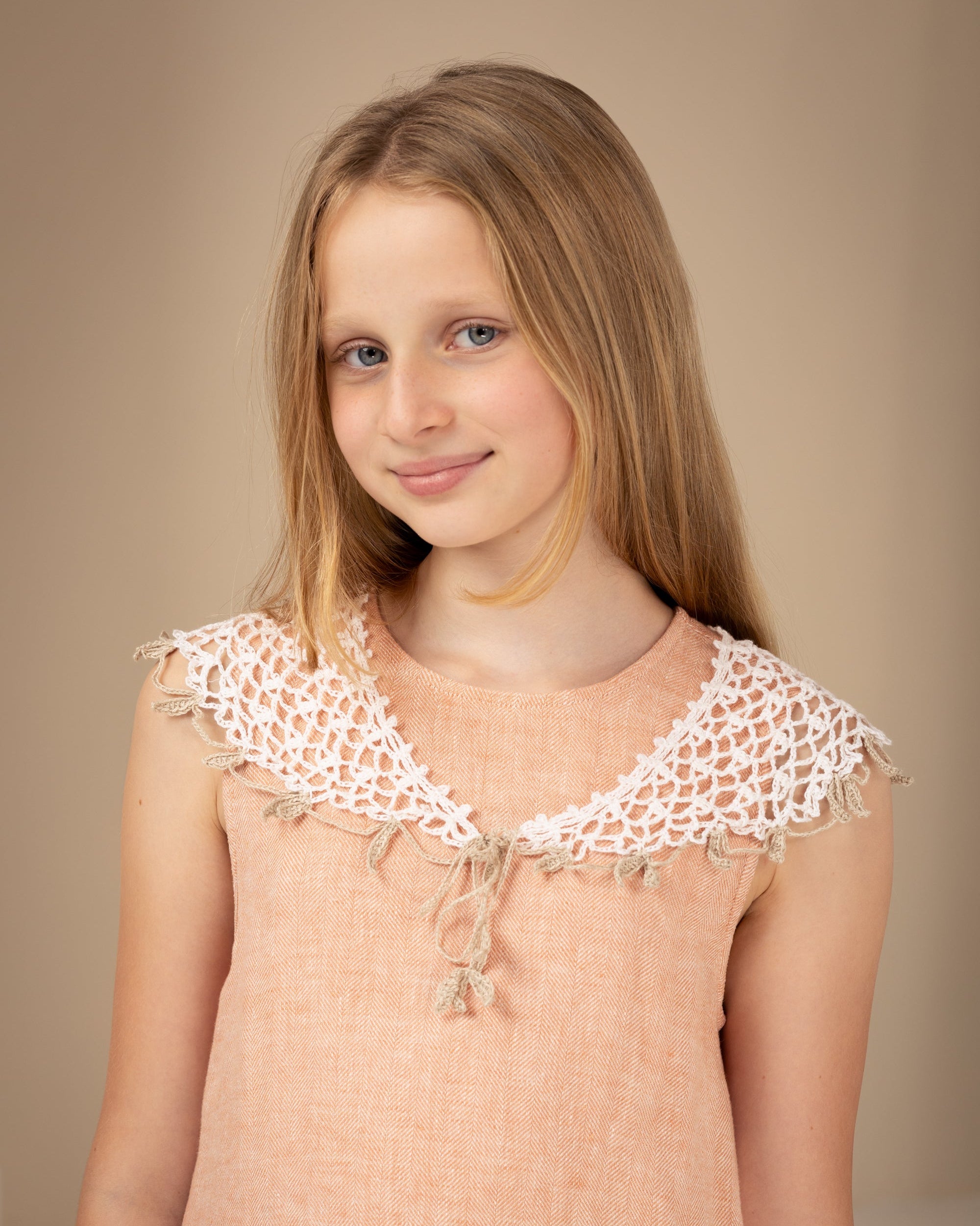 Young girl wearing a peach linen dress with crocheted linen collar against a beige background