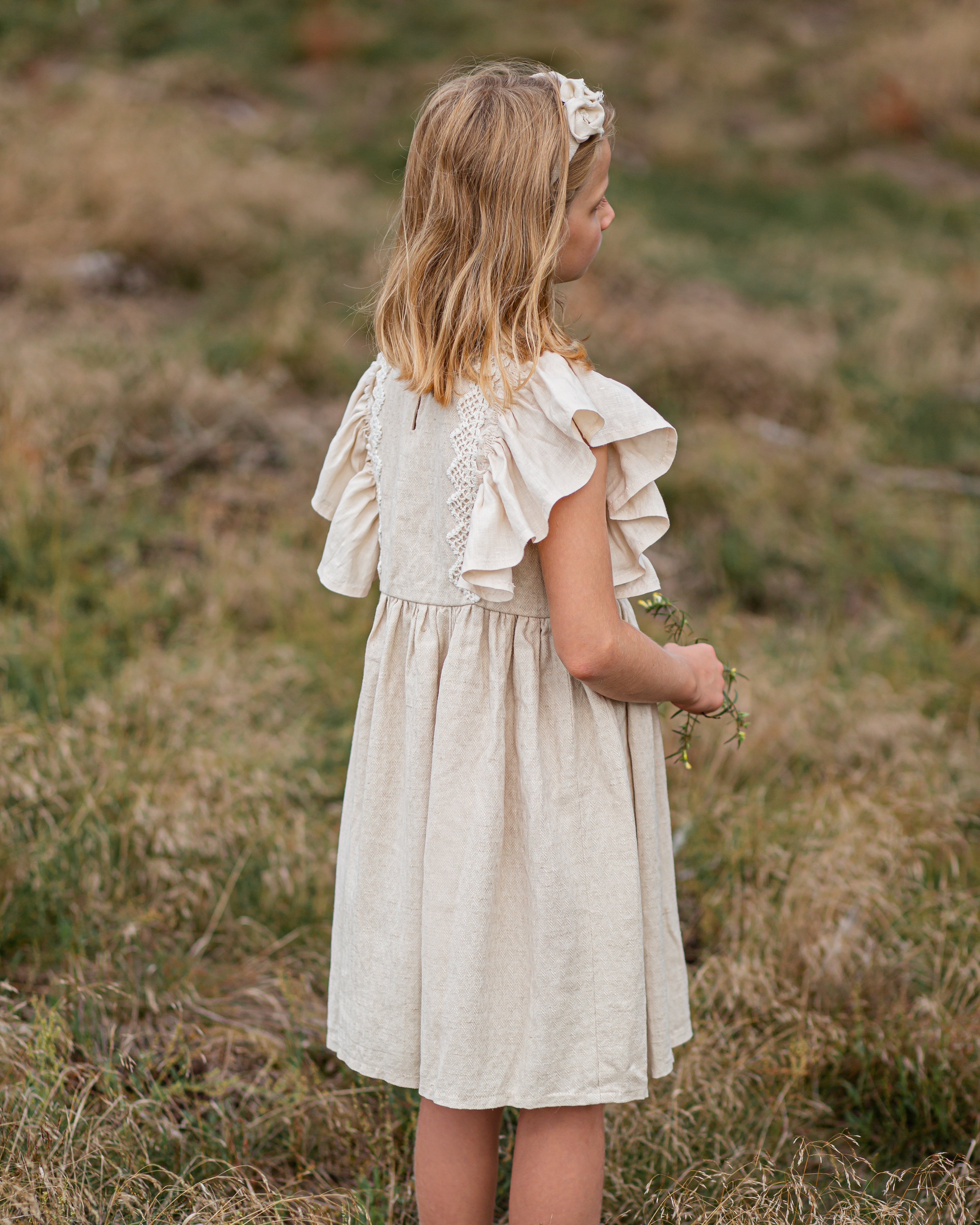 Young girl in a beige linen dress with crochet lace standing in a grassy field