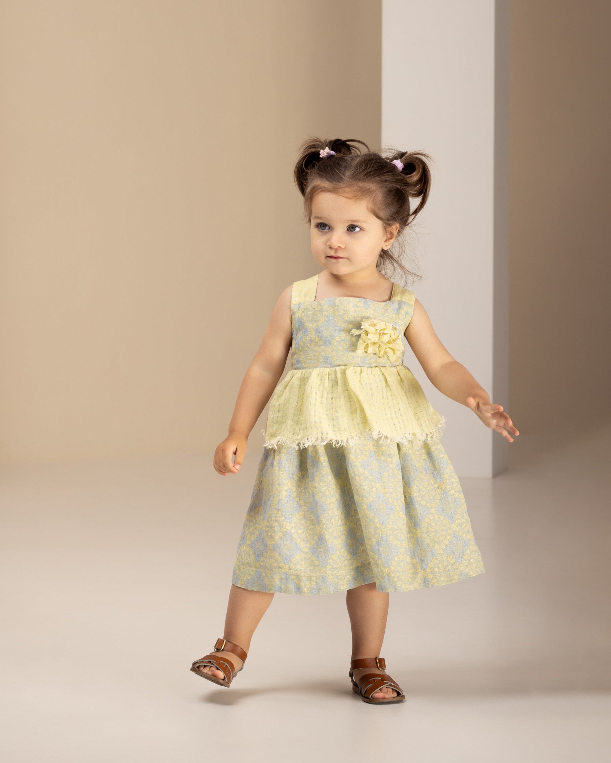 Little girl in a floral linen dress standing against a plain background