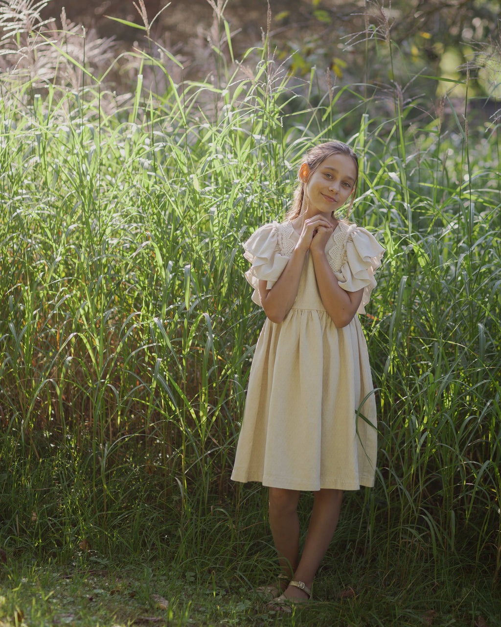 Young girl in a beige linen dress with crochet lace standing in tall grass
