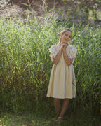 Young girl in a beige linen dress with crochet lace standing in tall grass