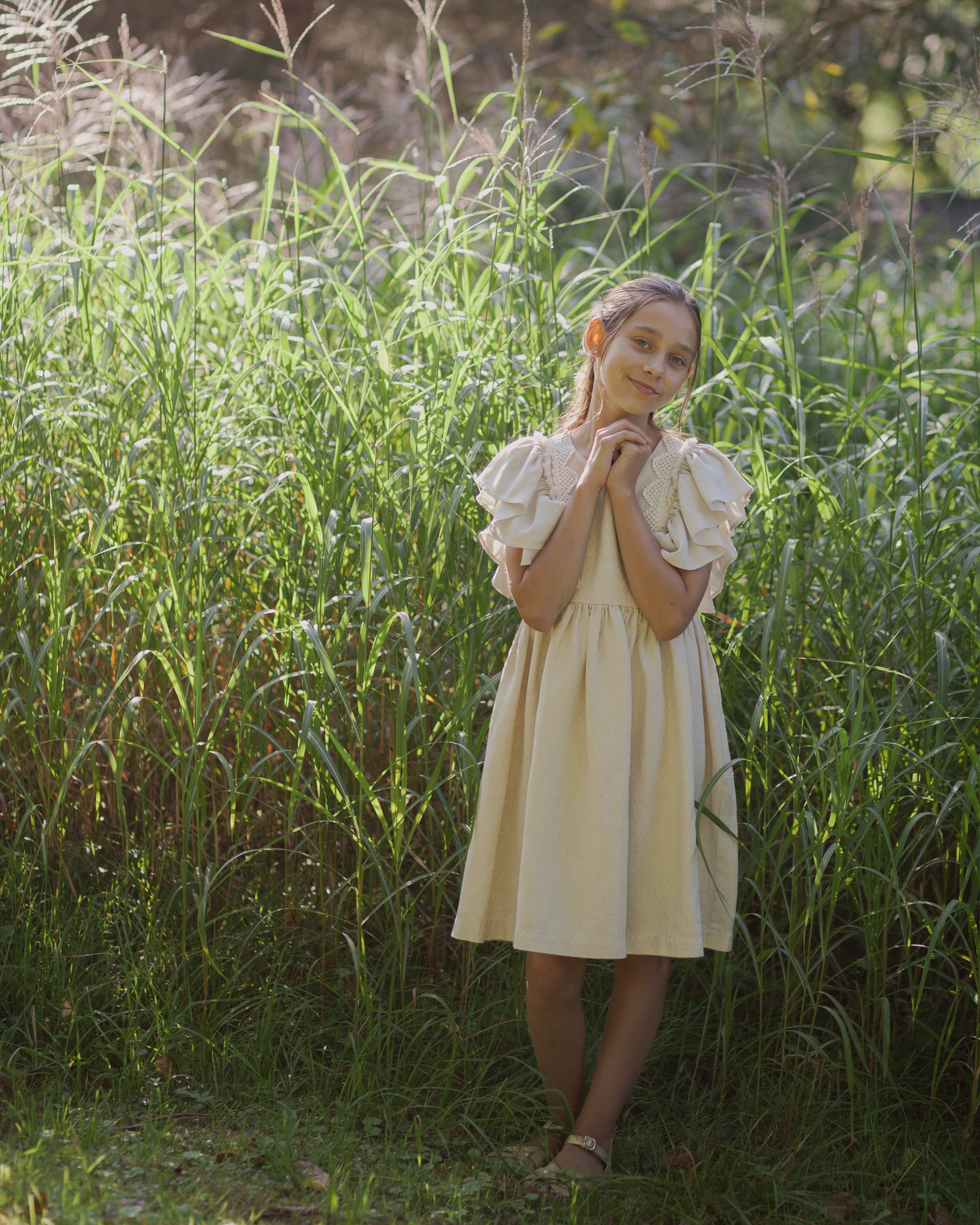 Young girl in a beige linen dress with crochet lace standing in tall grass