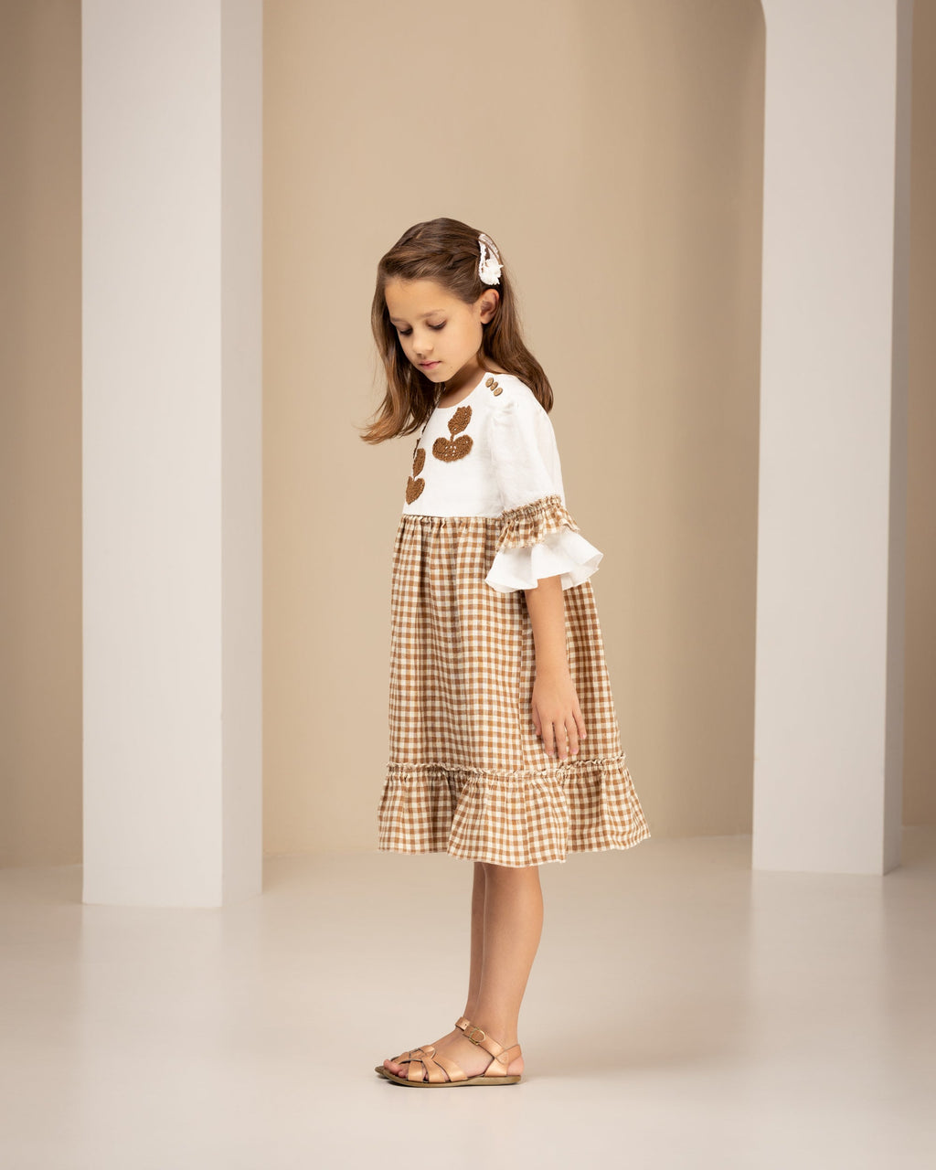 Young girl in a checkered linen dress standing in an archway with a neutral background