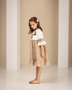 Young girl in a checkered linen dress standing in an archway with a neutral background