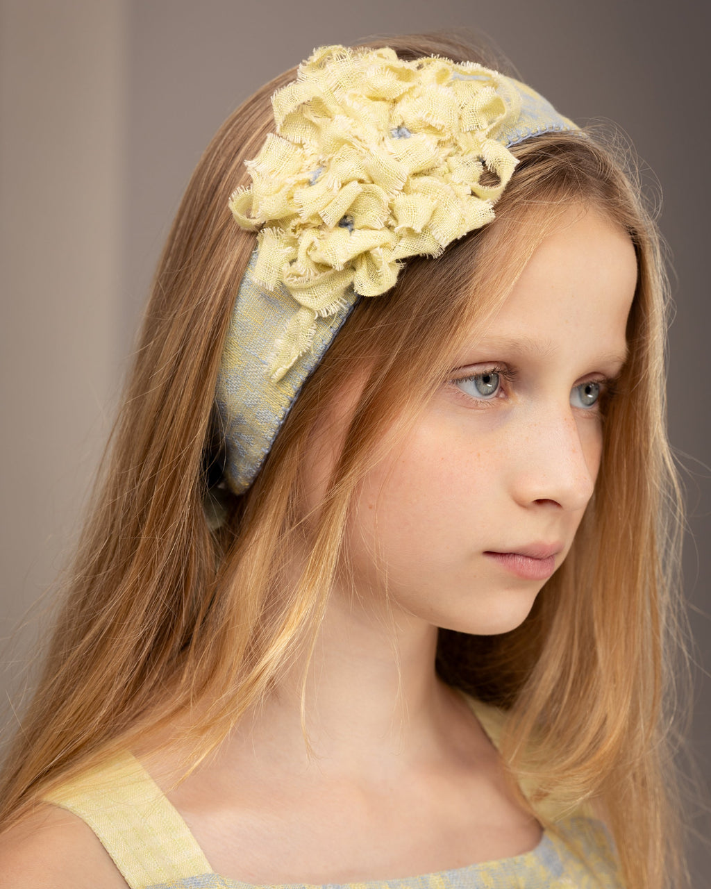 Young girl wearing a decorative tie-back headband with flowers from fabric scraps against a neutral background