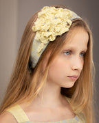 Young girl wearing a decorative tie-back headband with flowers from fabric scraps against a neutral background
