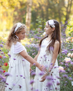 Two young girls in white linen dresses standing in a field of flowers.