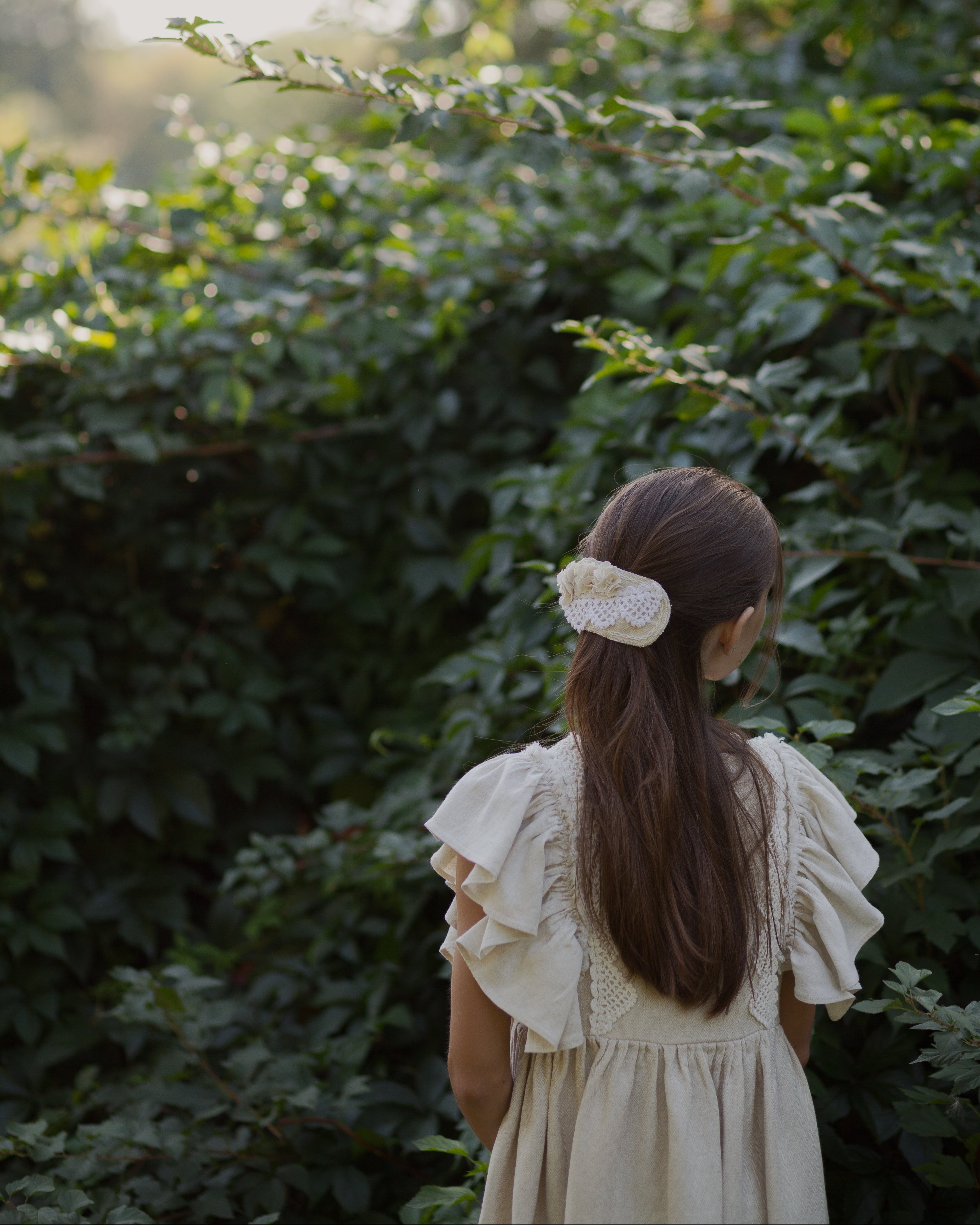Young girl in a beige linen dress standing in front of green foliage