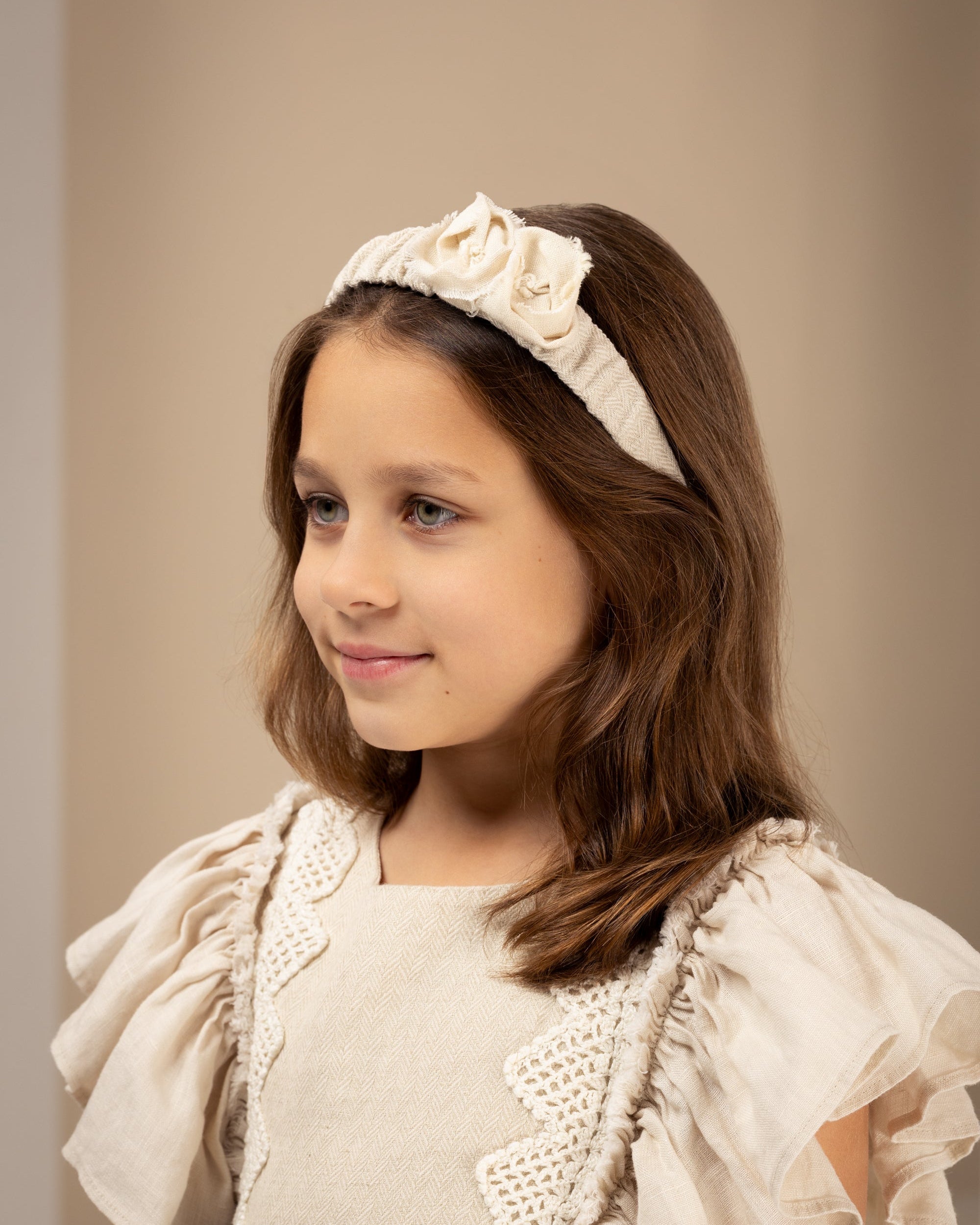Young girl wearing a decorative linen headband with flowers against a plain background
