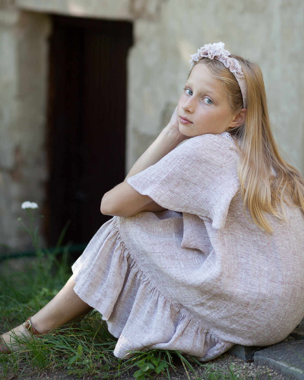Young girl in a beige linen dress sitting on the ground with a rustic background