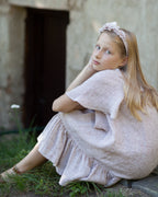 Young girl in a beige linen dress sitting on the ground with a rustic background