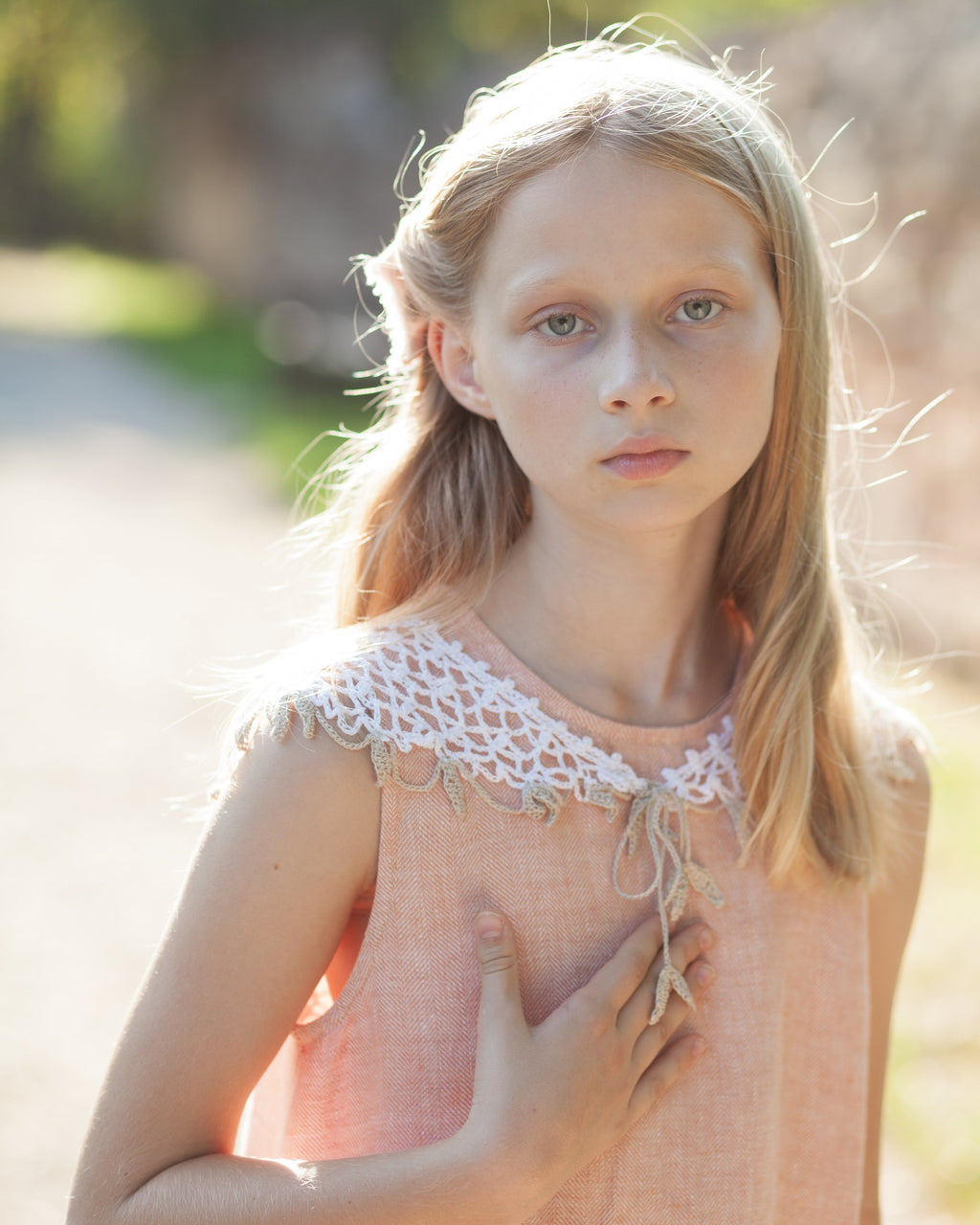 Young girl with blonde hair wearing a peach linen dress with crochetes linen collar in a natural setting