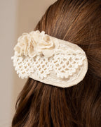 White linen hair clip with crocheted lace and fabric flowers on brown hair against a neutral background