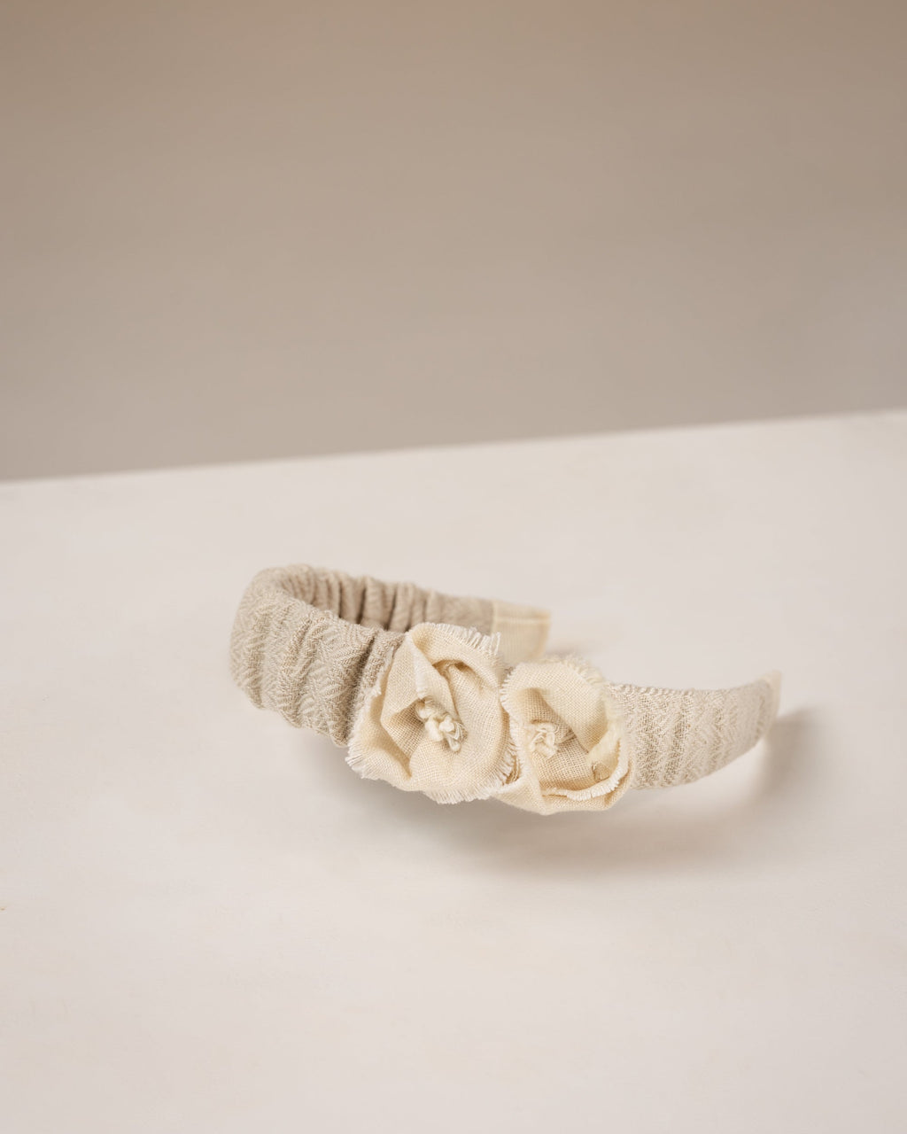 Beige linen headband with flowers from fabric embellishments on a white surface