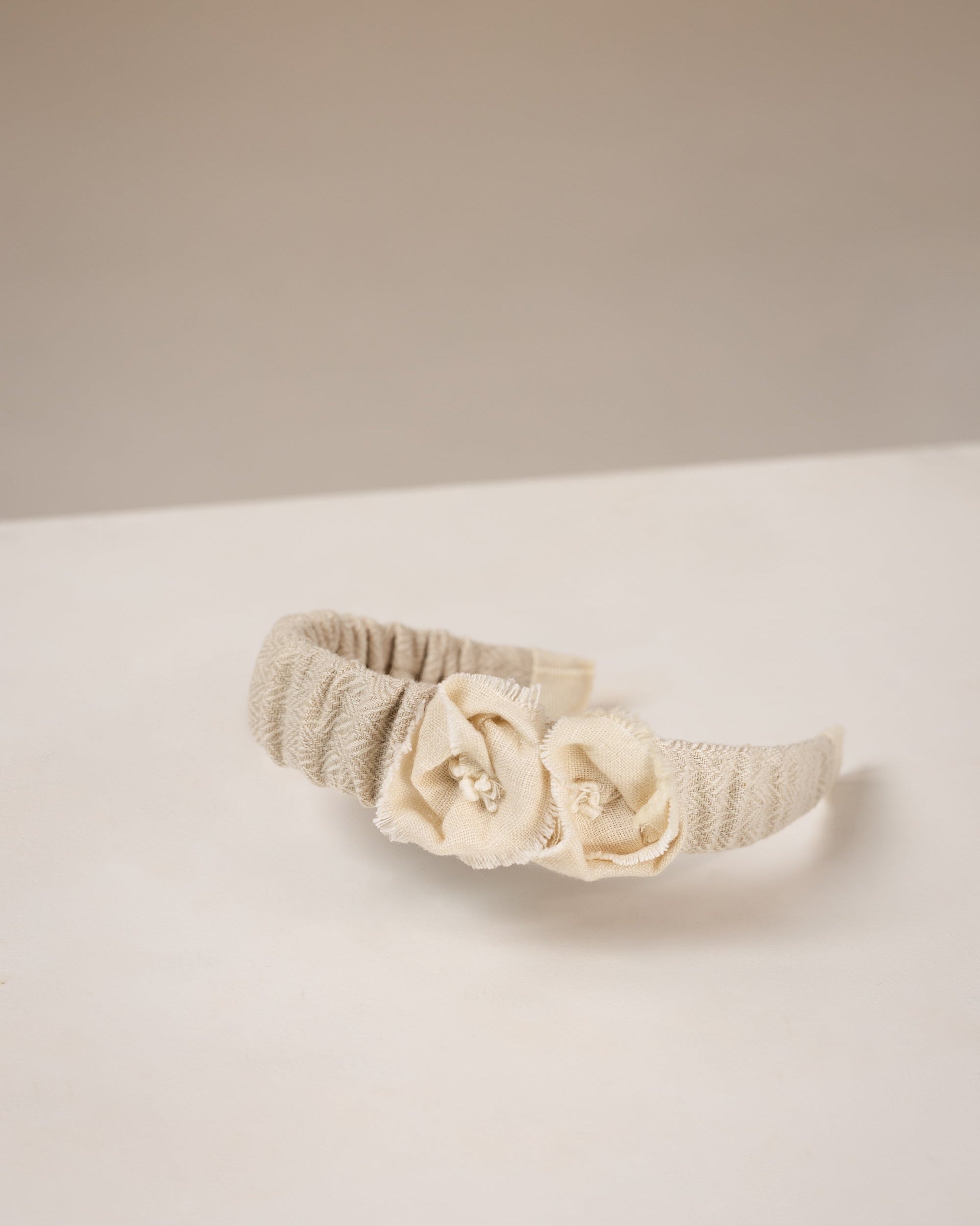 Beige linen headband with flowers from fabric embellishments on a white surface
