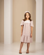 Young girl in a pink linen dress standing in an archway with a neutral background