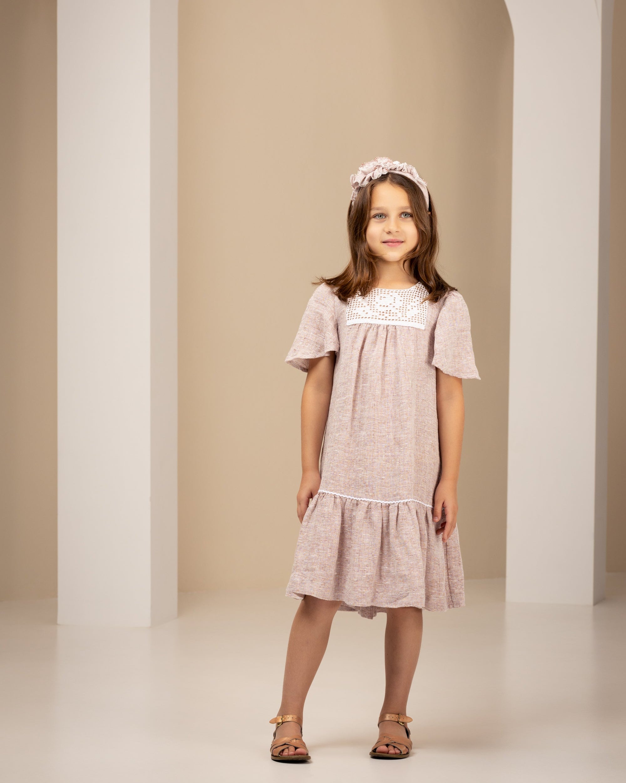 Young girl in a pink linen dress standing in an archway with a neutral background