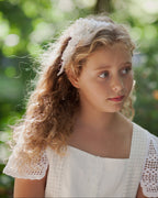 Young girl with curly hair wearing a white lace headband against a blurred green background