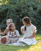 Group of children with linen dresses sitting on a blanket outdoors, enjoying a picnic.