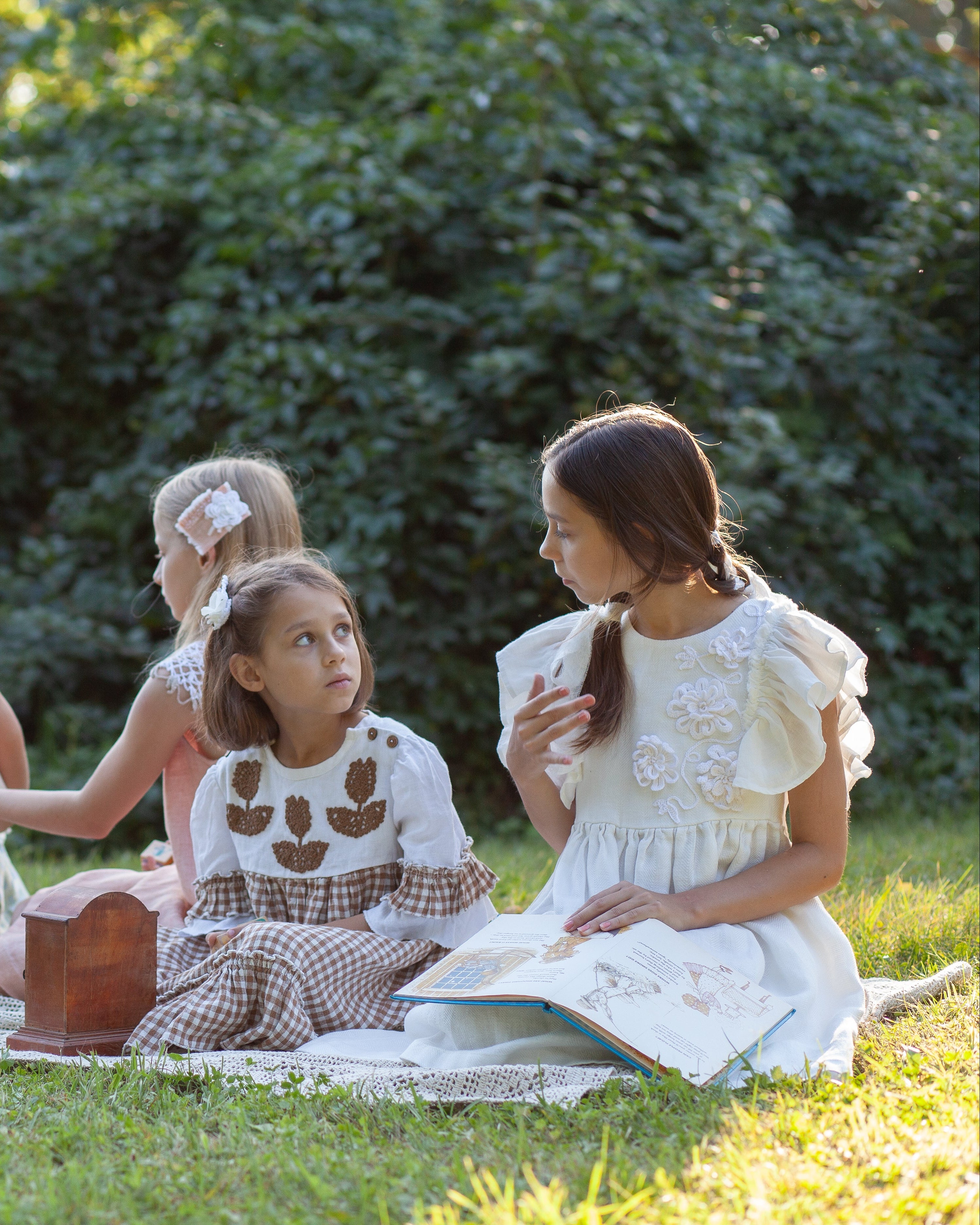 Group of children with linen dresses sitting on a blanket outdoors, enjoying a picnic.