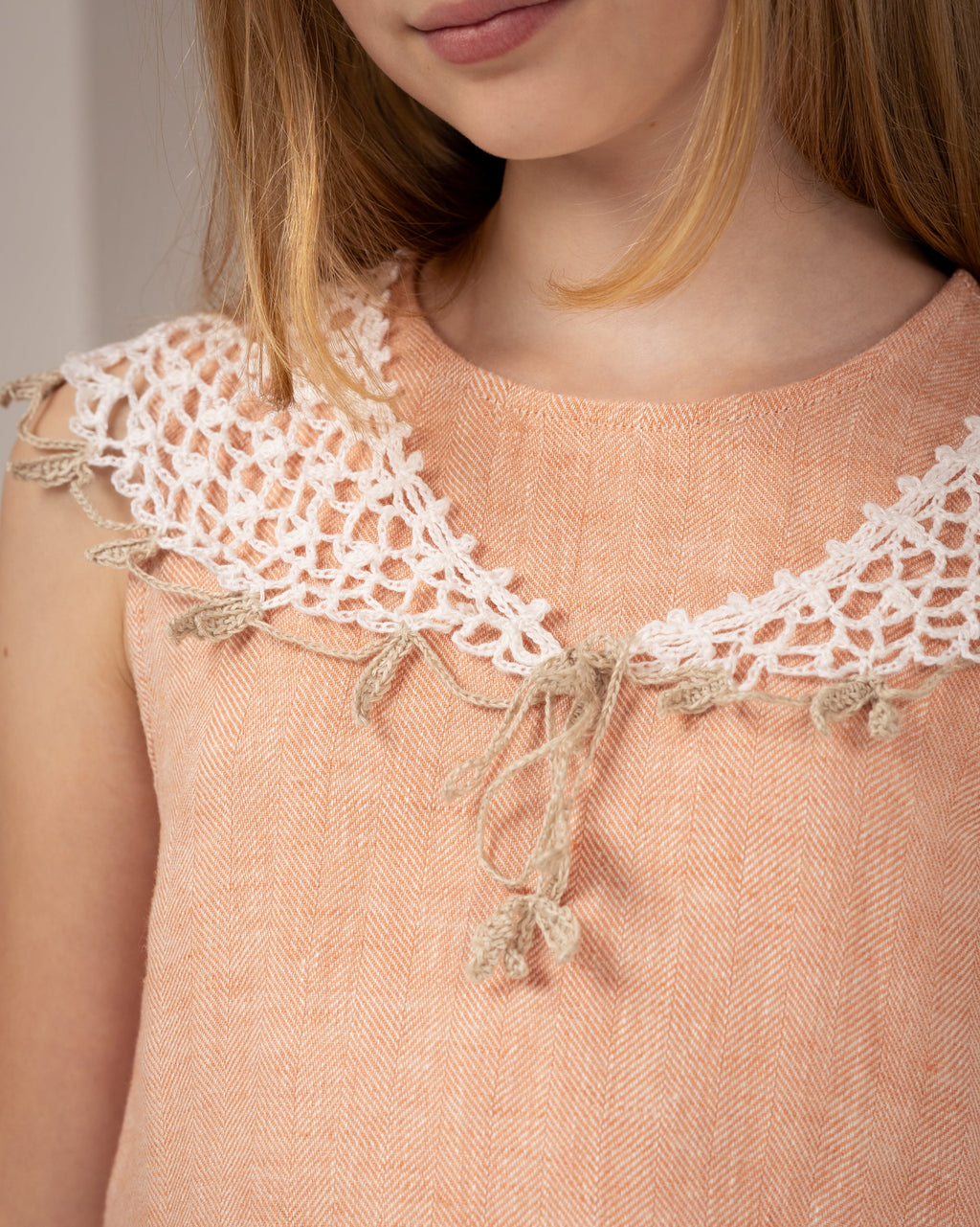 Close-up of a crocheted white linen collar and sleeveless linen peach color dress