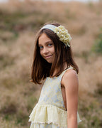 Young girl in a light yellow linen dress with floral patterns standing in a field.