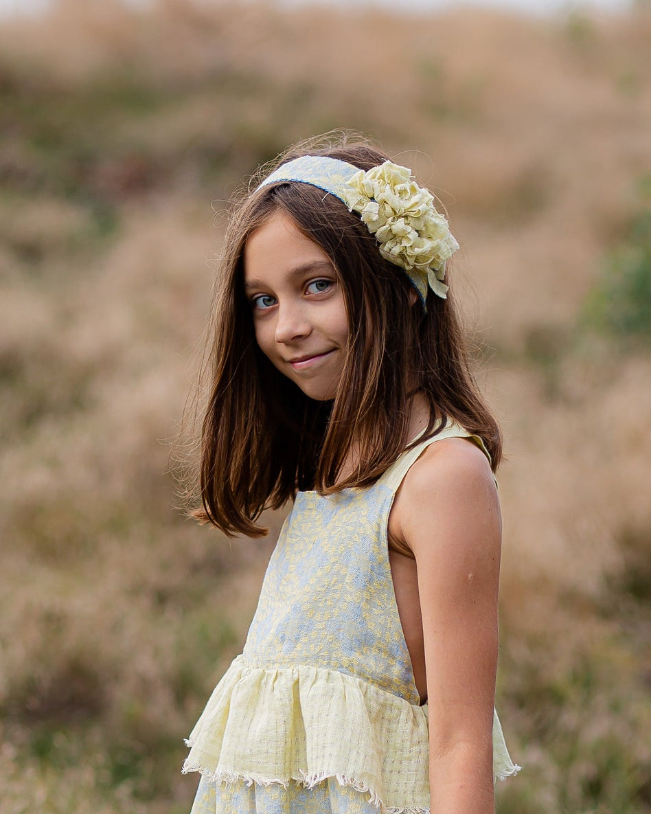 Young girl in a light yellow linen dress with floral patterns standing in a field.