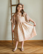 Young girl in a linen peach dress standing in a room with wooden flooring and a ladder.